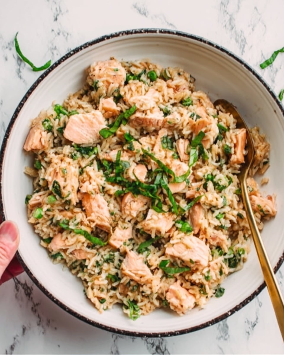 The image shows a white bowl with a thin black rim filled with a salmon rice dish. The bottom layer consists of light brown cooked rice mixed with small green vegetable pieces. On top, there are chunks of soft, pink cooked salmon evenly spread across the rice. Fresh green herbs are scattered over the dish for garnish. A woman's hand is partly visible, holding a golden spoon placed inside the bowl. The bowl sits on a white marbled surface. Photo taken with an iphone --ar 4:5 --v 7