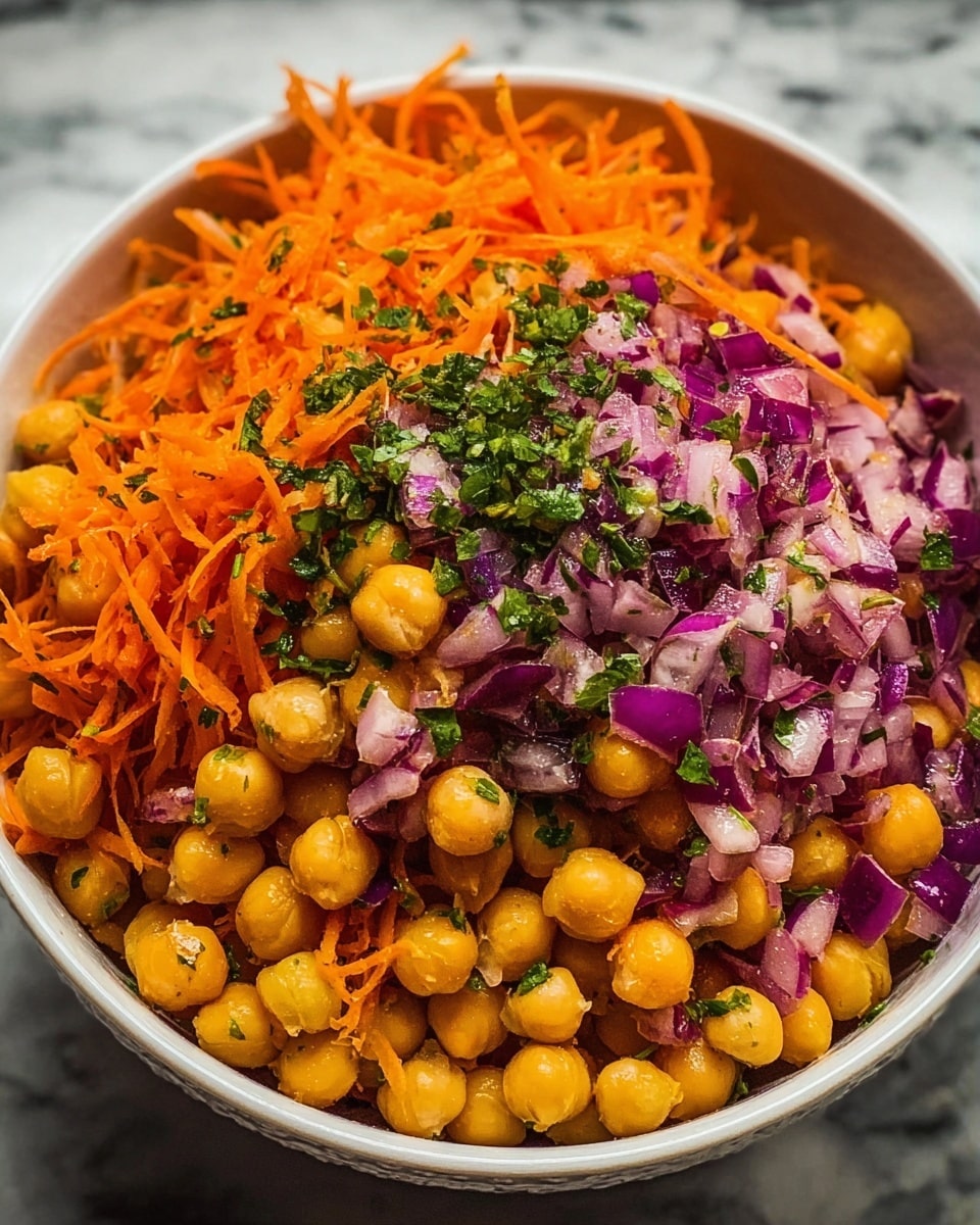 A close-up of a white bowl filled with a vibrant salad made of three main layers: the base layer is golden chickpeas with a smooth round texture, the middle layer consists of bright orange shredded carrots with a thin, stringy texture, and the top layer shows small pieces of purple-red chopped onion mixed with green chopped herbs scattered throughout. The ingredients are well-mixed but still show distinct color and texture contrasts, all resting on a white marbled surface in soft lighting. photo taken with an iphone --ar 4:5 --v 7