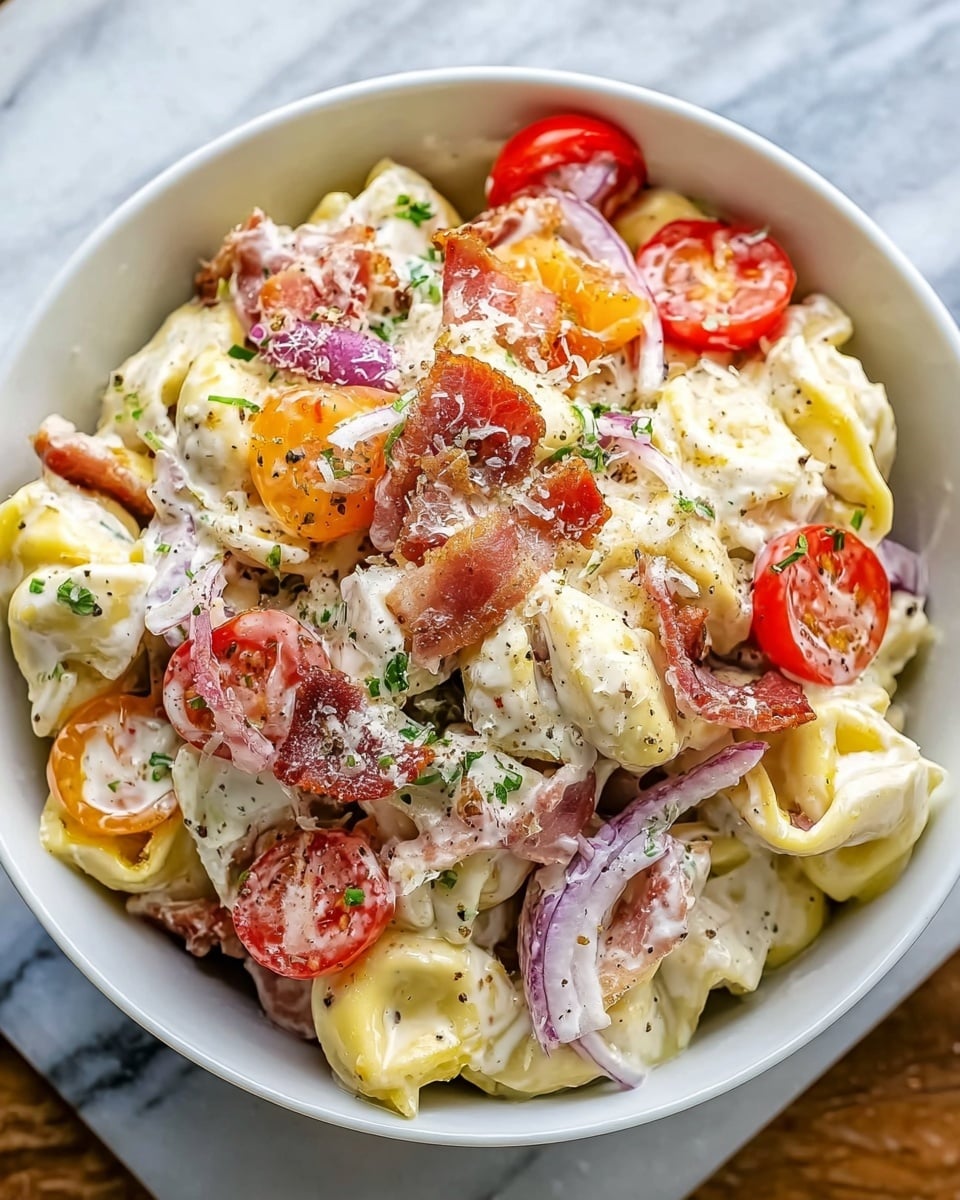 The dish is a creamy tortellini salad served in a white bowl, sitting on a white marbled texture. The bottom layer is filled with yellow cheese-filled tortellini pasta covered in a thick white cream sauce. Scattered on top are slices of bright red cherry tomatoes and thin pieces of crispy light brown bacon. Thin slices of purple onion and some green herbs add fresh color throughout. The whole salad is lightly sprinkled with finely grated white cheese and small cracked black pepper bits. Photo taken with an iphone --ar 4:5 --v 7