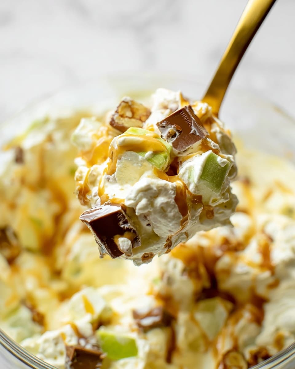 A close-up view of a creamy fruit salad in a white bowl, showing a mix of chunky layers with diced green apple pieces, orange-colored fruit segments, and chocolate-covered nut or candy chunks. These layers are coated heavily in a thick white cream or mayonnaise-like dressing, making the salad look rich and textured. The bowl sits on a white marbled surface with soft lighting highlighting the glossy texture of the cream and the mix of colors inside the bowl. photo taken with an iphone --ar 4:5 --v 7