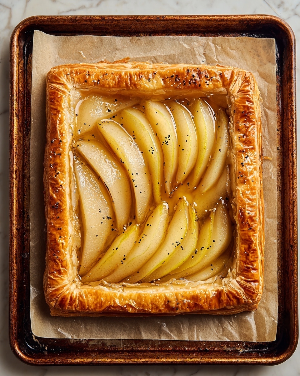 A square puff pastry tart with a golden brown, flaky crust that is thick and well-risen at the edges. Inside the crust, there is a layer of shiny, light brown caramel sauce spread evenly across the base. On top of the caramel, there are three neat rows of thinly sliced apple pieces, arranged in slightly overlapping layers, showing yellowish-white flesh with a slight golden tint from cooking. The tart sits on a piece of parchment paper on a dark baking tray. photo taken with an iphone --ar 4:5 --v 7