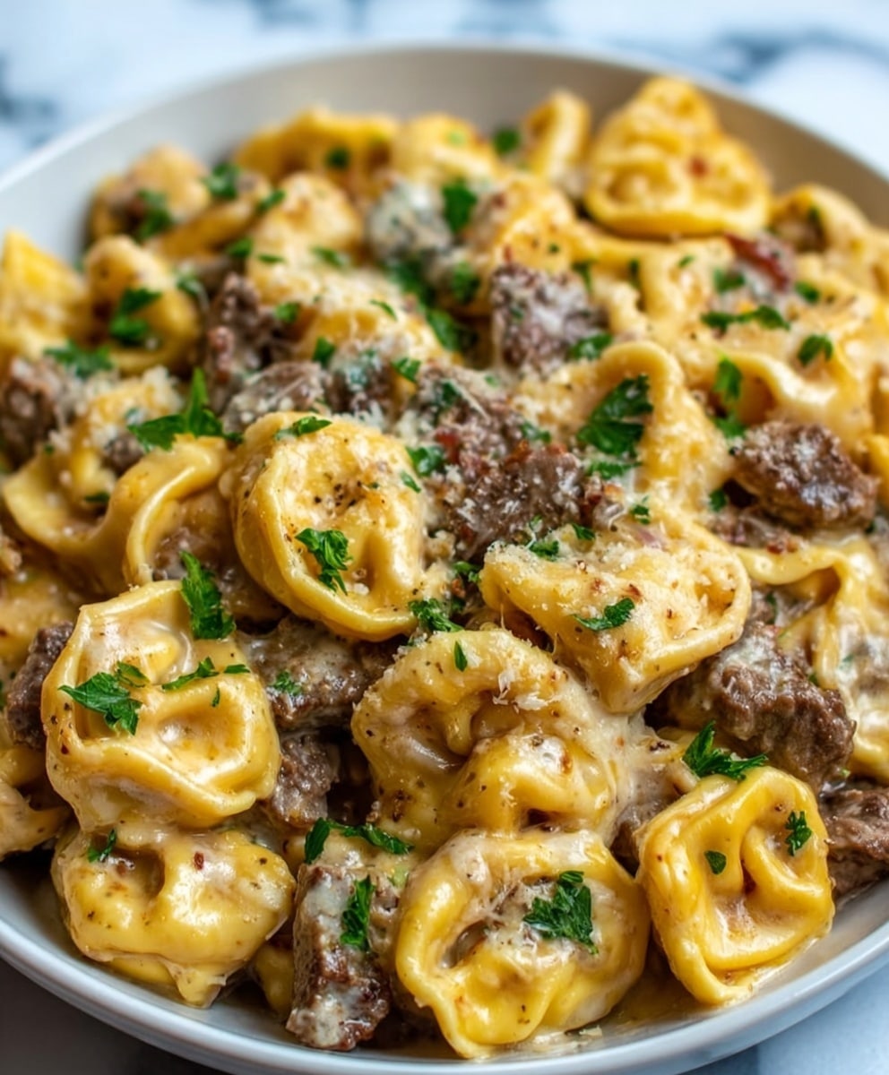 A close-up of a white bowl filled with creamy Philly cheesesteak tortellini. The dish shows multiple layers of golden-yellow tortellini pasta stuffed and folded neatly, covered in rich, melted cheese sauce. Small pieces of browned steak are scattered evenly throughout the pasta, adding a dark brown color contrast. Fresh green parsley leaves are sprinkled on top, adding a pop of color. The texture looks creamy and smooth with soft pasta and tender steak chunks. The bowl sits on a white marbled surface. Photo taken with an iphone --ar 4:5 --v 7