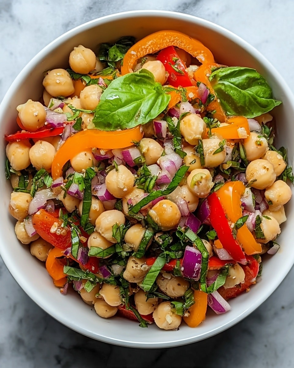 A white bowl filled with a colorful salad made of three main visible layers: the bottom layer has round, light beige chickpeas; on top of them are thin slices of bright orange bell pepper and small pieces of red onion, showing a purple shade; the salad is mixed with fresh green leaves of basil and small chopped herbs dotted throughout, adding texture and color contrast. The salad appears fresh, vibrant, and slightly glossy, suggesting a light dressing. The bowl is placed against a white marbled texture. photo taken with an iphone --ar 4:5 --v 7