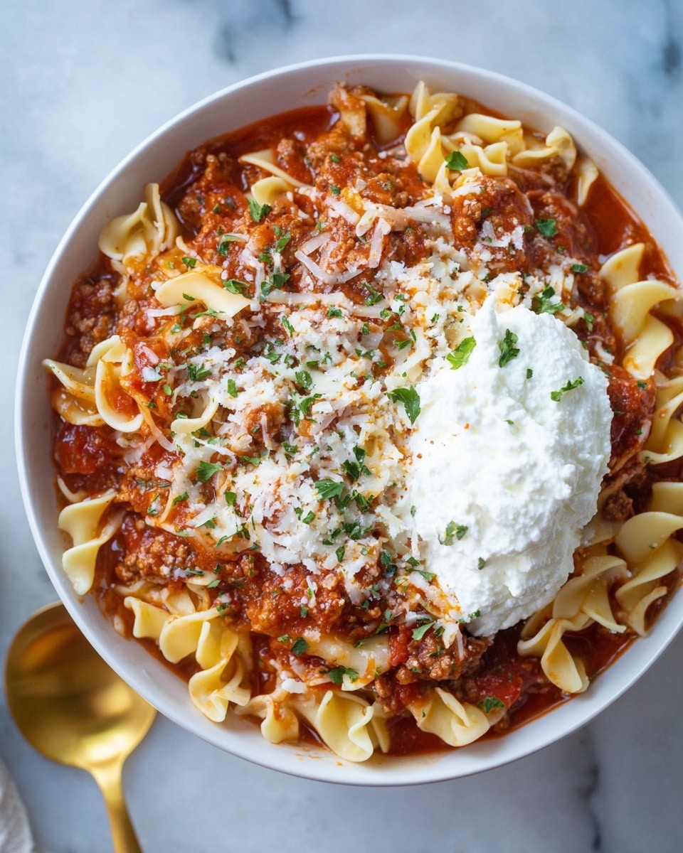 A white bowl is filled with a layered pasta dish consisting of soft, wavy, light yellow noodles mixed with a chunky red tomato sauce that has ground meat throughout. Shredded white cheese is sprinkled across the top, along with small pieces of fresh green herbs scattered over the dish. Resting on one side of the bowl is a large dollop of smooth white ricotta cheese. The bowl sits on a white marbled surface with part of a gold spoon visible at the lower left corner. Photo taken with an iphone --ar 4:5 --v 7