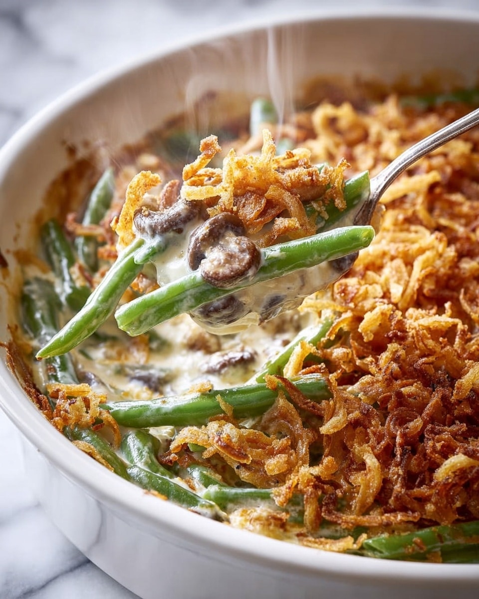 A close-up view of a creamy green bean casserole in a white dish, showing three layers: the bottom layer with tender green beans of bright green color, the middle layer with a smooth white cream sauce coating the beans and small mushroom pieces mixed in, and the top layer with a crunchy, golden brown fried onion topping spread evenly. There is steam rising from the dish, and a silver spoon is scooping a portion, revealing the creamy texture underneath. The dish is placed on a white marbled surface. photo taken with an iphone --ar 4:5 --v 7