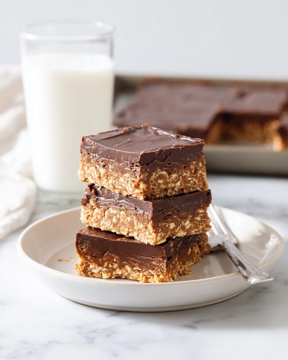 Three square bars are stacked in the middle of a round white plate on a white marbled surface. Each bar has two main layers: a thick, shiny, and smooth dark brown chocolate layer on top and a textured, crumbly golden oat layer on the bottom. The top bar shows a few cracks on its edge. Behind the plate, there is a clear glass filled with white milk and in the far back, part of a tray with more bars is visible. A silver fork lies on the edge of the plate. Photo taken with an iphone --ar 4:5 --v 7