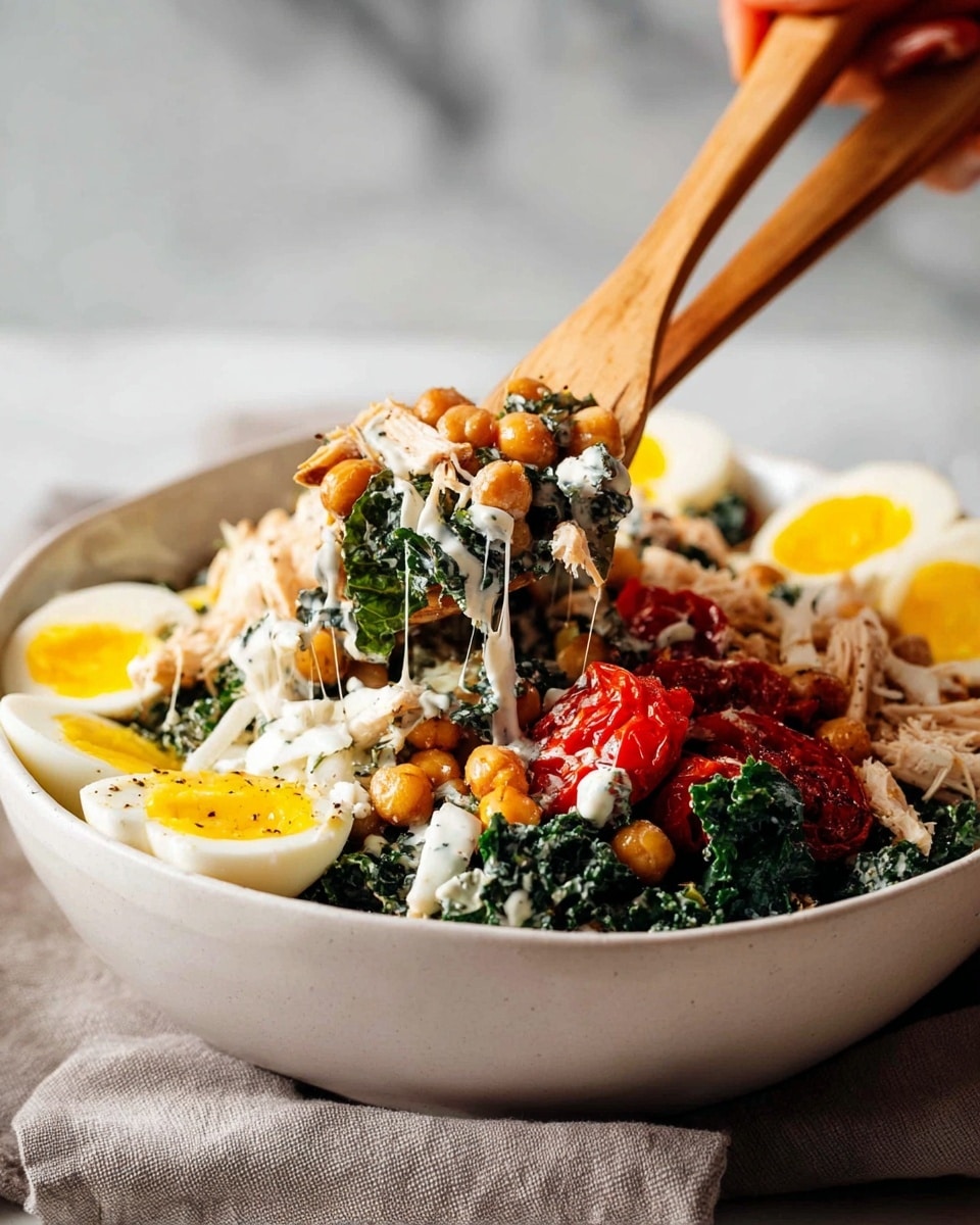A white bowl filled with a layered salad: the base consists of chopped dark green kale leaves, topped with golden brown roasted chickpeas and pieces of shredded white chicken. There are halved boiled eggs with bright yellow yolks placed around the edge of the bowl. Red roasted tomatoes and sliced white onions add color contrast. A creamy white dressing is drizzled over the top, adding texture and shine. Two wooden salad utensils are lifting a mix of the salad from the bowl with a woman's hand visible holding the utensils. The bowl is placed on a soft gray cloth against a white marbled surface background. photo taken with an iphone --ar 4:5 --v 7