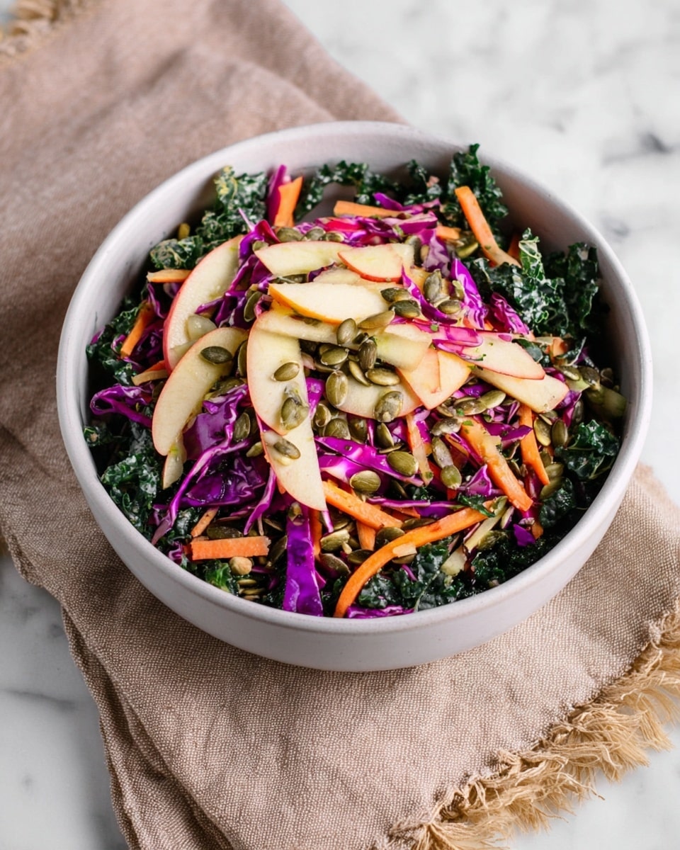 A white bowl filled with a colorful salad containing multiple layers: dark green chopped kale at the base, thin light orange carrot sticks scattered throughout, purple shredded cabbage mixed in, and light beige apple slices layered on top along with some green pumpkin seeds and light brown sunflower seeds sprinkled across. The salad has a fresh, glossy texture and is placed on a light brown cloth with frayed edges, all set against a white marbled surface. photo taken with an iphone --ar 4:5 --v 7