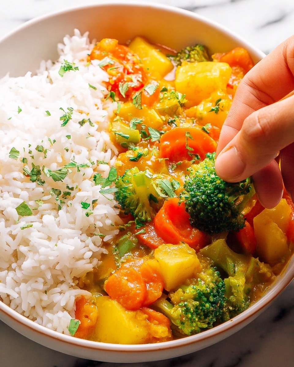 A close-up view of a white bowl filled with two main layers: a fluffy white rice layer on the left side and a colorful vegetable curry layer on the right. The curry layer includes bright green broccoli florets, orange carrots, yellow potato chunks, and a glossy sauce covering all the vegetables. Small green herbs are sprinkled on top of both the rice and vegetables. A woman's hand is placing a piece of broccoli into the bowl against a white marbled surface background. photo taken with an iphone --ar 4:5 --v 7